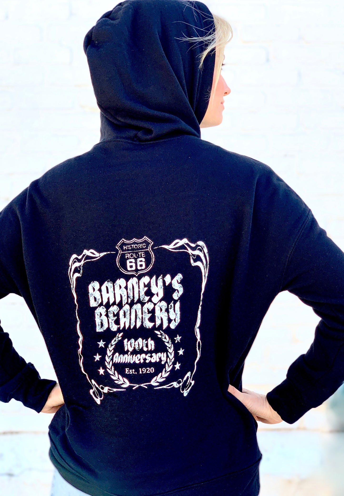 Woman from behind wearing a black hoodie with 100 year logo on the back  